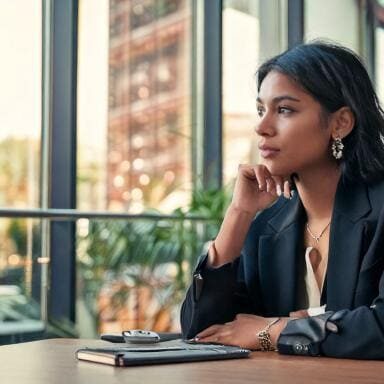 A woman thinking through her next steps in an office setting while looking out the sunny windows.