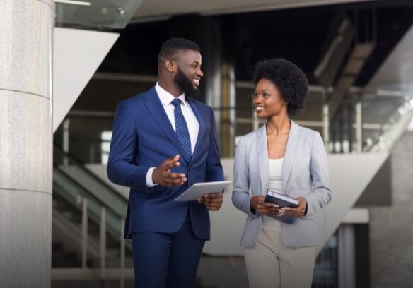 Two coaches, a man and a woman, are walking and smiling in a modern office building.