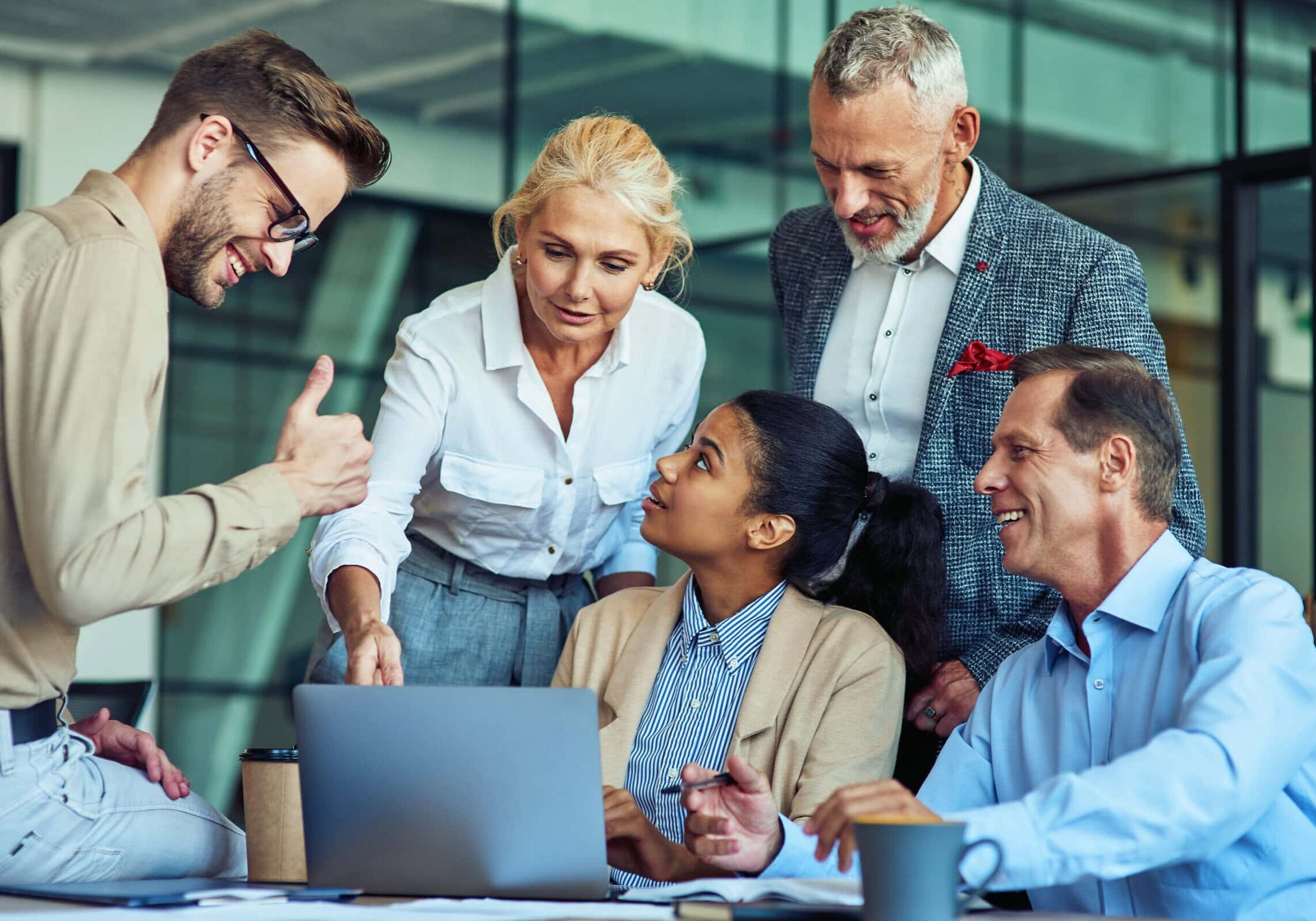 Five professionals engaged in an interactive coaching session around a laptop, demonstrating teamwork and leadership development.