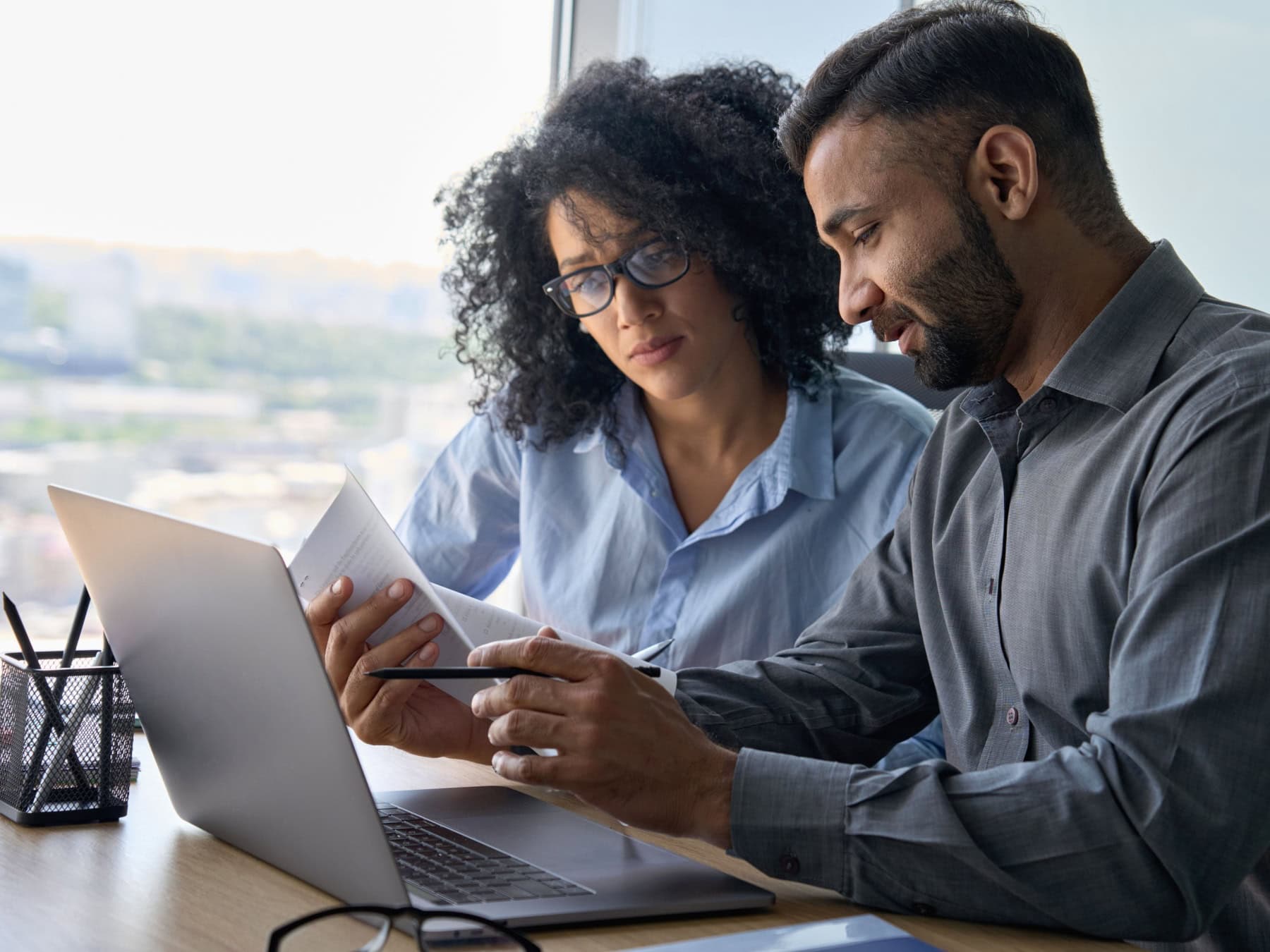 A man and woman review information on a computer screen in a casual office.