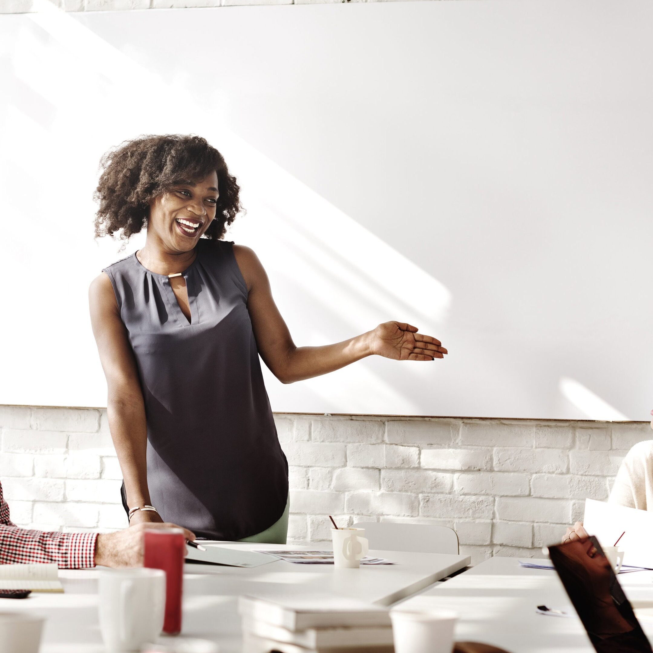 A smiling professional woman leads a group coach workshop, engaging with attendees in a collaborative and positive environment.