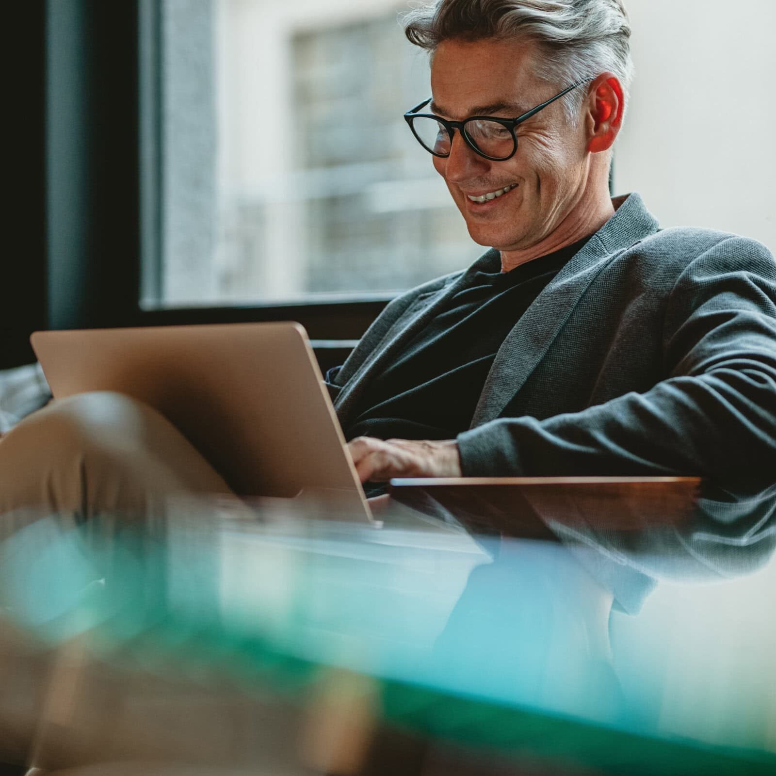 A silver-haired professional coach working comfortably focused credential updates on a laptop in a modern, relaxed office setting.