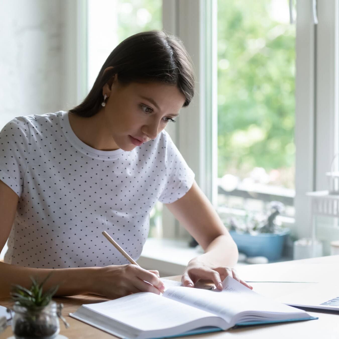 A woman is writing in a notebook at a home office.