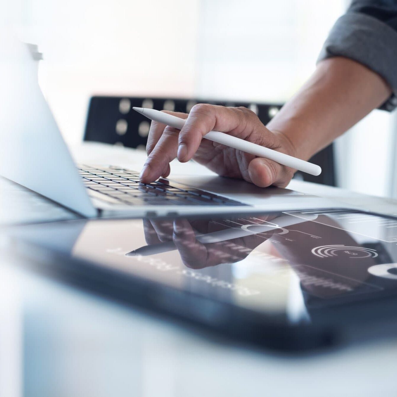 person with one hand on a laptop keyboard with an apple pencil and their other hand on an ipad screen