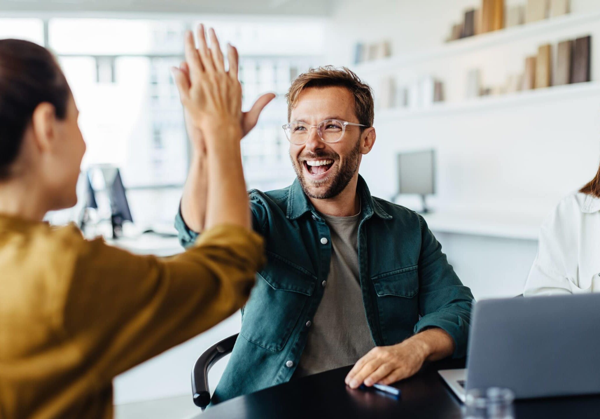 man high-fives woman at a table with another smiling next to him