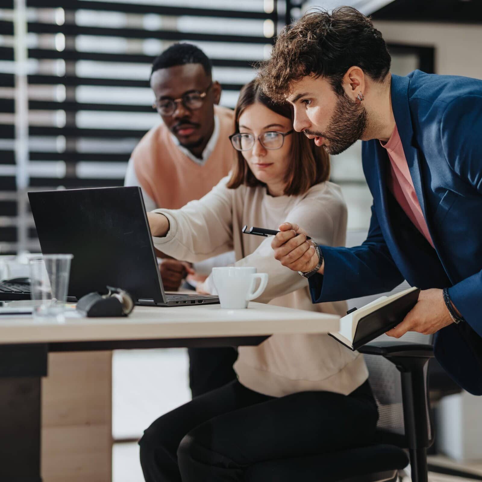 three people at a laptop with one pointing to something on a laptop screen