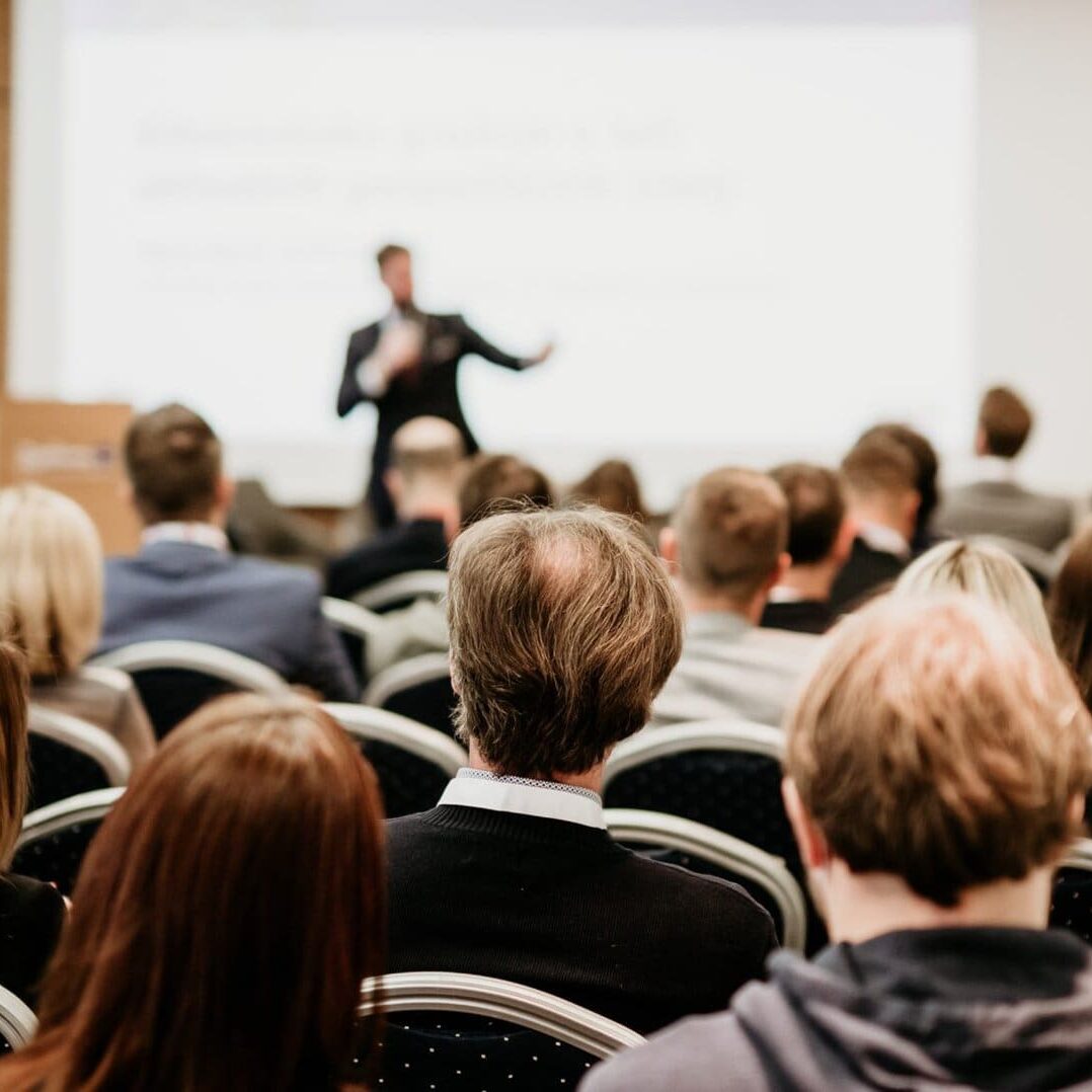 large conference hall with speaker at the front giving a presentation